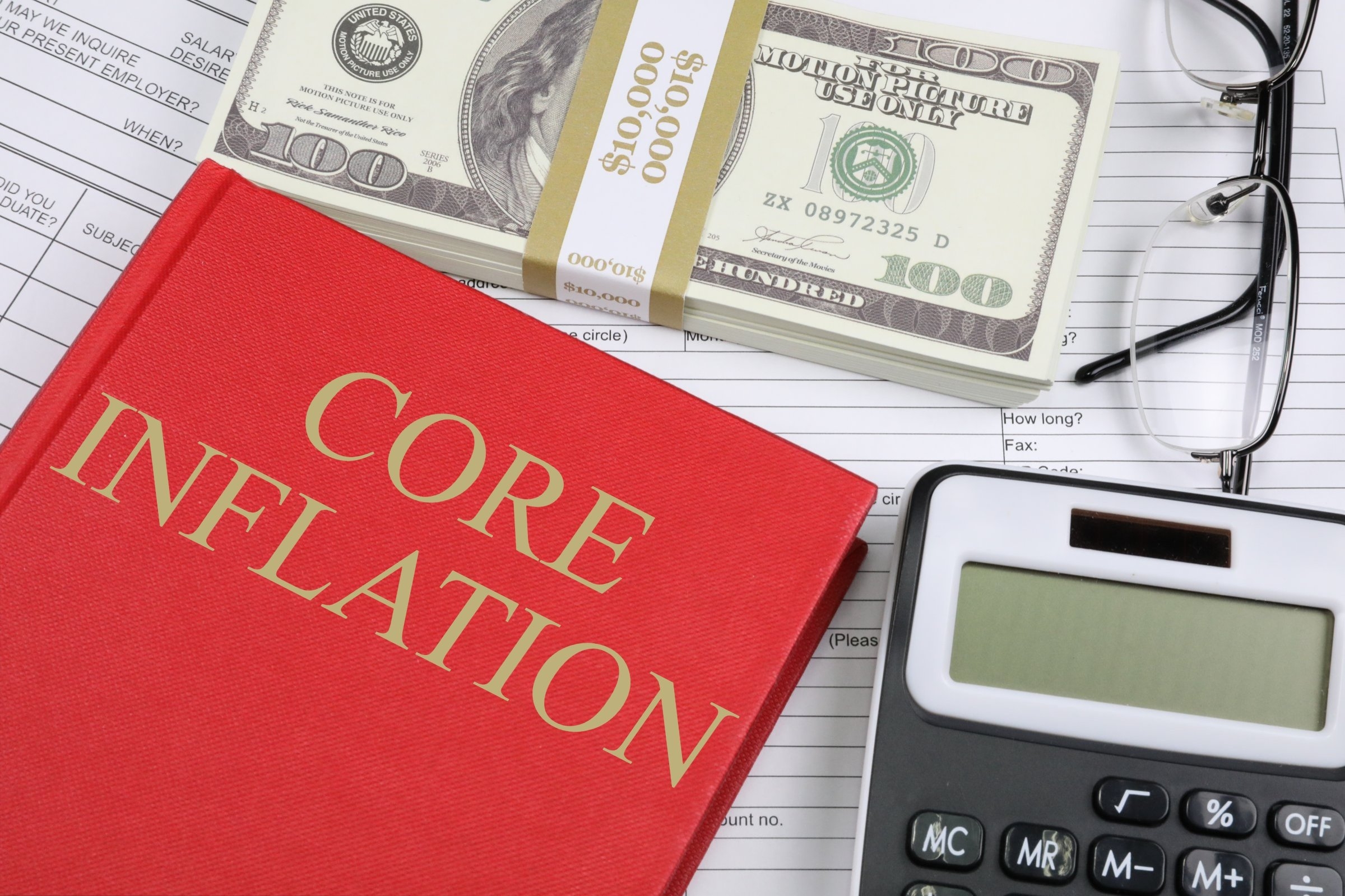 a stack of money next to a book on inflation and a calculator